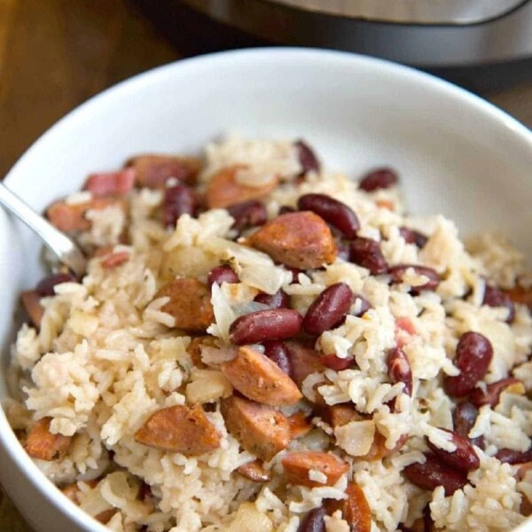 Bowl of rice with kidney beans and sausage slices, showcasing a delightful rendition of instant pot red beans and rice, with a pressure cooker in the background.
